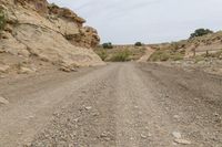 a dirt road with rocks and a rock face in the background, with a hill on either side