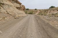 a dirt road with rocks and a rock face in the background, with a hill on either side