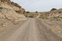 a dirt road with rocks and a rock face in the background, with a hill on either side