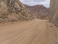 a small vehicle traveling across a barren road between some large rocks and boulders on one side