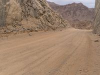 a small vehicle traveling across a barren road between some large rocks and boulders on one side