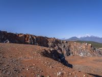 a person standing on top of a dirt field near a hillside and mountain range, next to a crater and rock formation