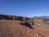 a person standing on top of a dirt field near a hillside and mountain range, next to a crater and rock formation