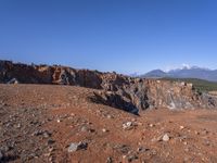 a person standing on top of a dirt field near a hillside and mountain range, next to a crater and rock formation