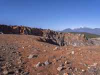 a person standing on top of a dirt field near a hillside and mountain range, next to a crater and rock formation