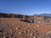 a person standing on top of a dirt field near a hillside and mountain range, next to a crater and rock formation