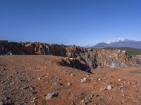 a person standing on top of a dirt field near a hillside and mountain range, next to a crater and rock formation