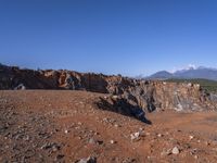 a person standing on top of a dirt field near a hillside and mountain range, next to a crater and rock formation