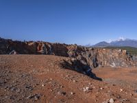 a person standing on top of a dirt field near a hillside and mountain range, next to a crater and rock formation