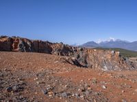 a person standing on top of a dirt field near a hillside and mountain range, next to a crater and rock formation