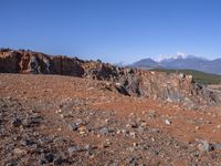 a person standing on top of a dirt field near a hillside and mountain range, next to a crater and rock formation