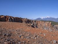 a person standing on top of a dirt field near a hillside and mountain range, next to a crater and rock formation