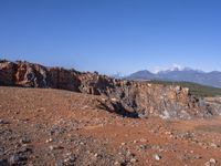 a person standing on top of a dirt field near a hillside and mountain range, next to a crater and rock formation