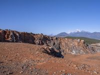 a person standing on top of a dirt field near a hillside and mountain range, next to a crater and rock formation