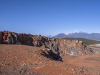 a person standing on top of a dirt field near a hillside and mountain range, next to a crater and rock formation