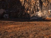 an orange truck on rocky ground next to rock formation and rocks with sun coming through