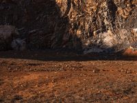 an orange truck on rocky ground next to rock formation and rocks with sun coming through