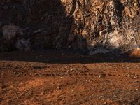 an orange truck on rocky ground next to rock formation and rocks with sun coming through