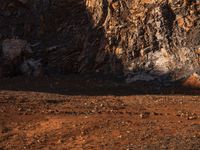 an orange truck on rocky ground next to rock formation and rocks with sun coming through