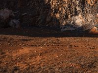 an orange truck on rocky ground next to rock formation and rocks with sun coming through