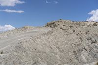 a dirt and gravel road runs up a hill in the desert with a car parked at the edge