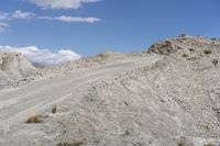 a dirt and gravel road runs up a hill in the desert with a car parked at the edge