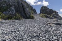 a small rocky road on top of a mountain with clouds overhead it is in the daytime