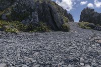 a small rocky road on top of a mountain with clouds overhead it is in the daytime