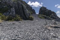 a small rocky road on top of a mountain with clouds overhead it is in the daytime