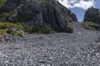 a small rocky road on top of a mountain with clouds overhead it is in the daytime