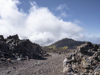 the trail is surrounded by rocks and trees and clouds behind it and the view of the mountains