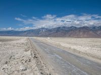 a dirt road in the middle of nowhere, with mountains in the distance and sparse land below