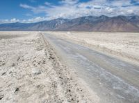 a dirt road in the middle of nowhere, with mountains in the distance and sparse land below