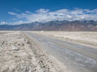 a dirt road in the middle of nowhere, with mountains in the distance and sparse land below