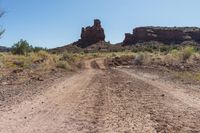 a dirt road in the desert between tall rocks and scrublands near a dry creek