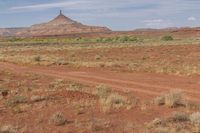 a couple riding horses in the desert by the mountains with dirt roads and sparse scrub land