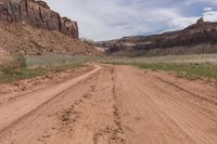 dirt road next to red canyon with green grass and a sign on it that reads