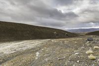 a dirt road through a barren terrain area with rocks and grass around it and two mountains in the distance