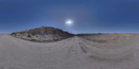 a sunny day at the end of a dirt road, with a half moon in the sky