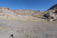 large rocky and gravel area with sparse trees, bushes, and sand in the foreground