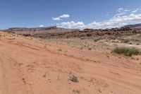 a red dirt road in the middle of nowhere in the desert with bushes and rocks in the background