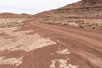 a dirt road surrounded by small bushes on the side of a rocky hill in a desert