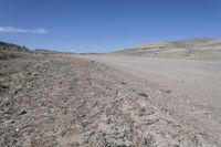 a dirt road is surrounded by some hills and desert like terrain as the vehicle sits on it