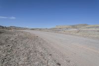 a dirt road is surrounded by some hills and desert like terrain as the vehicle sits on it