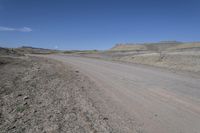 a dirt road is surrounded by some hills and desert like terrain as the vehicle sits on it