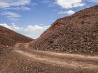 the dirt road is winding along the rocky hills covered in rocks and gravels, on which a few large piles are seen