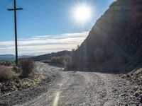 a narrow gravel road with rocks, grass and telephone pole in the background and mountains