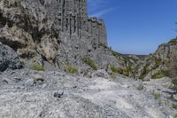 there are many rocks that have been eroded by the cliff side and some grass growing out on each one