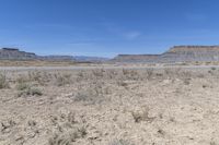 a wide expanse of dirt with a few plants in it and hills in the distance