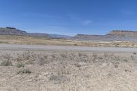 a wide expanse of dirt with a few plants in it and hills in the distance